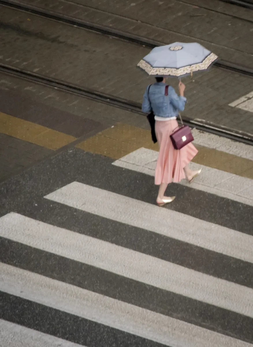 Woman with a pale umbrella and pink skirt crossing tram tracks